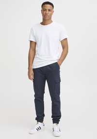 Vit kortärmad t-shirt ihop med marinblå cargobyxor med sidofickor, elastiska muddar och svartvita sneakers.
