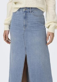 Jupe en denim bleu clair avec une fente avant, taille haute et fermeture à bouton standard. Dispose de poches cousues et d'une texture lisse.