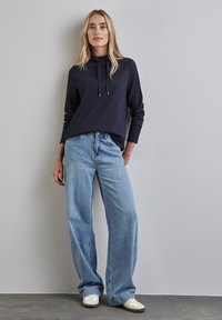 Marynarski, prążkowany top z długim rękawem z troków, zestawiony z jasnoniebieskimi, szerokimi spodniami dżinsowymi i białymi sneakersami. Minimalistyczny design z luźnym krojem.