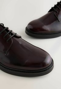 Dunkelburgunderfarbene Leder-Schnürschuhe mit polierter Oberfläche, schwarzen Sohlen und dezenten Nähdetails entlang der Kanten.