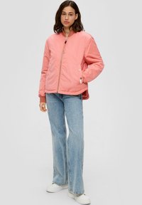 Chaqueta bomber rosa con cierre de cremallera, puños acanalados y bolsillos laterales, combinada con jeans acampanados de color azul claro y zapatillas blancas.