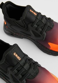 Black athletic shoes featuring a gradient design from purple to orange, with black laces, branded "GAMER," and textured soles with orange accents.