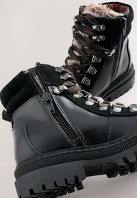 Black leather and suede hiking boots with silver hardware, textured grip soles, and fur accents at the collar; features zippers and laces.