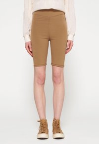 Shorts da bicicletta bordeaux in tessuto elasticizzato, con vita alta e orli cuciti, abbinati a sneakers beige alte.