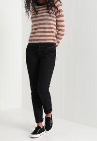 Czarne dopasowane spodnie w połączeniu z paskowanym swetrem z dzianiny w jasnoróżowym i brązowym kolorze, z długimi rękawami i czarnym wykończeniem. Stylizację dopełniają czarne sneakersy.