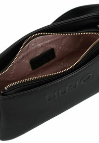 Bolso negro de cuero texturizado con el logo "Liu Jo" en relieve, cremallera dorada abierta que revela un interior de tela beige con estampado repetido de "Liu Jo".