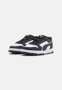 Black and white athletic shoes with a smooth leather upper, round toe, prominent lacing, and a textured rubber sole. Gold branding detail visible.
