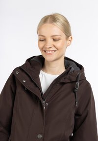 Brun vandtæt jakke med grå indvendig foring, justerbar hætte, frontlynlås og knaplukning. Casual design og pasform.