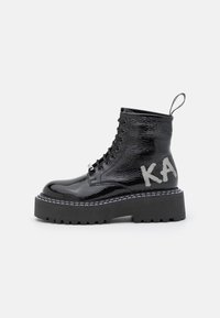 Black patent leather ankle boots with a chunky sole, lace-up front, and a pull tab, featuring a silver “KA” logo on the side.