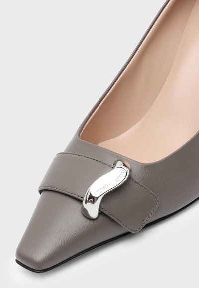 Chaussure en cuir grise à bout pointu avec une large bride et une boucle métallique argentée brillante sur le dessus. L'intérieur est beige.