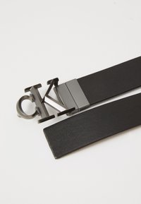 Zwarte leren riem met een gedurfde metalen CK-logo gesp, met een gladde textuur en een strakke vorm. Verstelbare lengte voor gemak.