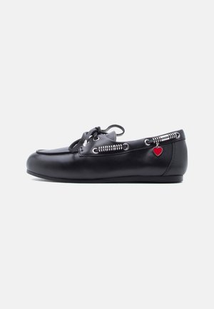 Chaussure bateau en cuir noir avec un design à lacets, des détails texturés, des accents en métal argenté et un charm en forme de cœur rouge sur le côté.