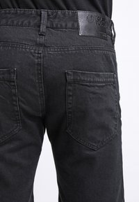 Svarta denimjeans med en åtsittande design, som har en texturerad yta, två bakfickor och en läderlogotyp på midjebandet.