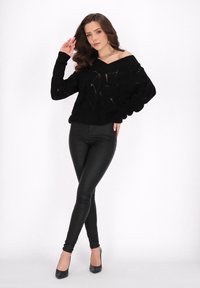 Maglione nero a maglia con design off-the-shoulder, tessuto testurizzato e maniche ampie, abbinato a leggings neri aderenti e tacchi alti.