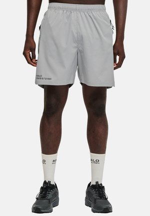 Shorts de sport gris avec une taille élastique, des poches latérales et des détails en texte noir. Associés à des chaussettes blanches et des chaussures de sport noires.