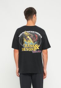 Zwarte katoenen t-shirt met een kleurraf vis-thema graphic op de achterkant, met tekst en een visontwerp in levendige kleuren.