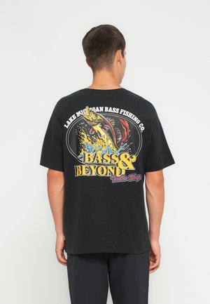 T-shirt en coton noir avec un graphique coloré sur le thème de la pêche au dos, affichant du texte et un motif de poisson dans des couleurs vives.