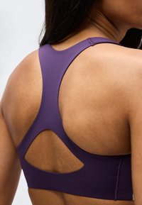 Κοντινό πλάνο ενός ατόμου που φοράει ένα μωβ αθλητικό σουτιέν racerback με γεωμετρικό άνοιγμα στην πλάτη.