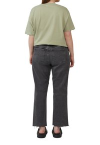 Oversized lichtgroene t-shirt gecombineerd met high-waisted zwarte denim jeans, met een afgesneden zoom en standaard achterzakken. Zwarte schoenen.