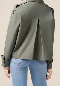 Olive green cropped jacket with shoulder epaulettes, buttoned cuffs, and a pleated back design. Paired with light blue fitted jeans.