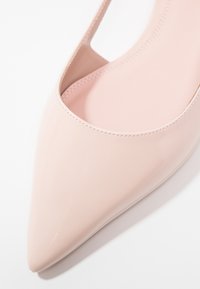 Ljusrosa lackpumps med spetsig tå och utskärning på sidan. Slät yta med minimala sömnadsdetaljer.