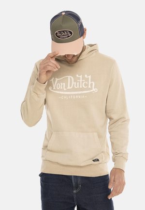 Sweat à capuche beige avec poche avant, arborant le logo blanc « Von Dutch California ». Assorti à une casquette trucker verte et rose, en tissu texturé.
