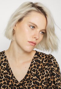 Blusa de estampado de leopardo com decote em V, mangas curtas em forma de puff e textura suave. Estilizada com cabelo loiro claro, solto e ondulado, e brincos de argola.