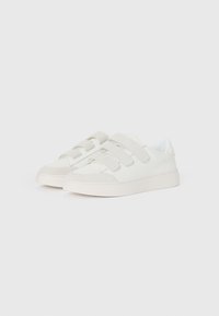 White sneakers with two velcro straps, smooth material, rounded toe, contrasting light gray suede accents on the front, and a thick sole.