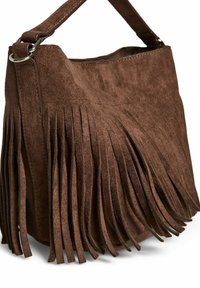 Brūns zamša rokassoma ar frēzējumu, noapaļota forma un izturīga siksna ar metāla aksesuāriem. Mīksta tekstūra uzlabo dizainu.