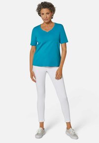 Turquoise T-shirt met korte mouwen en een V-hals, voorzien van een subtiele rand. Gecombineerd met witte slim-fit broeken en grijze sneakers. Eenvoudig ontwerp.