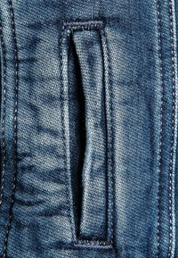 Close-up of a vertical slit pocket on blue denim fabric with visible stitching and seam details.