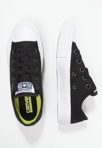 Černé plátěné tenisky s bílou gumovou podešví, kulatou špičkou, šesti otvory na šňůrky a zelenou vnitřní podšívkou. Obsahují branding Converse All Star.