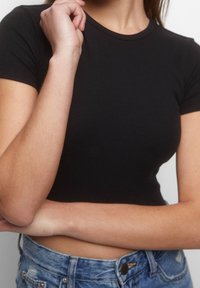 Haut court côtelé noir à manches courtes avec un col rond, associé à un short en denim bleu à taille haute avec une fermeture à boutons.