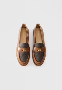 Een paar bruine leren en donkergepatroneerde Michael Kors instappers met een gouden MK-logo op de band, tentoongesteld op een witte achtergrond.