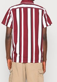 Kurzarmhemd mit vertikalen Streifen in Burgunderrot, Weiß und Schwarz. Das Material scheint leicht und mit einem lässigen Schnitt sowie klassischem Kragen zu sein.