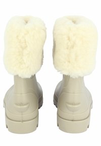 Beige rubberen laarzen met een fluffy crème nepbontkraag, ronde neus en een gestructureerde zool. Glad oppervlak met subtiele details aan de achterkant.