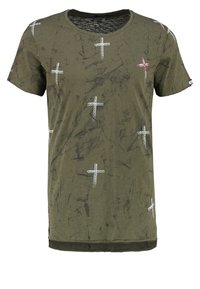 Oliivinvihreä puuvillainen T-paita, jossa on pyöreä kaula-aukko. Paita on koristeltu pienillä valkoisilla ja punaisilla ristikuvioilla sekä teksturoiduilla yksityiskohdilla. Lyhyet hihat.