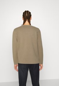 Maglione a maniche lunghe in verde oliva, texture a maglia, scollatura rotonda, vestibilità dritta, abbinato a pantaloni scuri. Sfondo chiaro.
