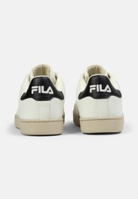 Vita sneakers med en texturerad läderöverdelen, svart hälaccent och beige gummisul. Har Fila-logotypen på baksidan.