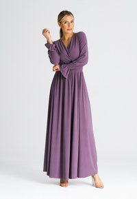 Długa, zwiewna sukienka z miękkiego fioletowego materiału o kroju kopertowym. Posiada długie rękawy, marszczoną talię i dzwonowate mankiety. Prosta, elegancka sylwetka.