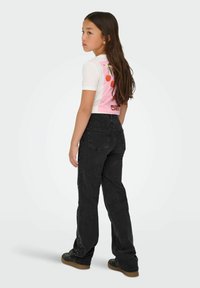 Camisa blanca de manga corta con un gráfico rosa que presenta cerezas; vaqueros anchos negros con adornos decorativos en los laterales.