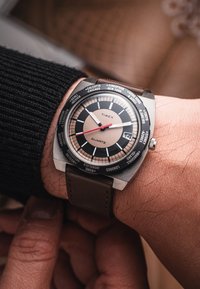 Timex Quarz Uhr mit schwarzem und bronzefarbenem Ziffernblatt, Edelstahlgehäuse, braunem Lederarmband und Städtenamen, die auf der Lünette eingraviert sind.