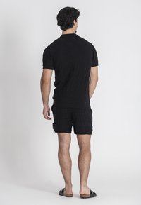 Completo in maglia nera composto da top a maniche corte e pantaloncini, con motivo testurizzato e sandali neri piatti con un accento maculato.