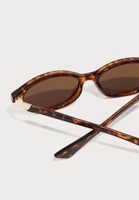 Schildpatt-sonnenbrille mit braunen Gläsern, ovalem Rahmen, glänzender Oberfläche und goldfarbener Akzentuierung an den Schläfen. Die Bügel sind schlank und gerade.