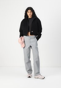Giacca nera cropped con zip, pantaloni grigi a gamba dritta e berretto rosa chiaro. Sneakers beige con dettagli grigi. Stile semplice e quotidiano.