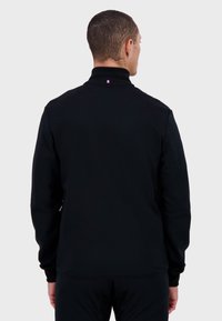 Felpa nera con zip, colletto alto e sottile accento tricolore sul retro del collo. Tessuto morbido, design aderente, maniche lunghe.