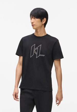 Schwarz Baumwoll-T-Shirt mit einem grafischen Design von "KL", das aus weißen Nieten besteht. Rundhalsausschnitt, kurze Ärmel, gerader Saum. Lässiger Schnitt.