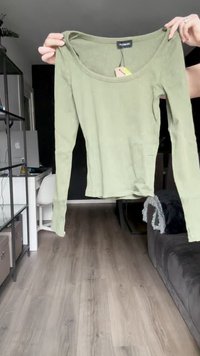 Olivno zelena dolga majica z rebrasto teksturo in izrezom v obliki kroga ter subtilnimi detajli na robu, ki je držana proti nevtralni ozadju.