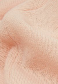 Weiches, strukturiertes Strickgewebe in Hellrosa, mit sichtbaren Rippen und leichten Variationen in der Dicke.