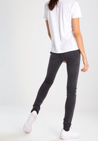 Šedé džínsy slim-fit vyrobené z bavlněné směsi, s středním pasem a jemnými švy, doplněné o jednoduché bílé tričko a bílé tenisky.